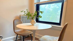Une petite table ronde avec deux chaises, une plante en pot et une vue sur les arbres par la fenêtre.