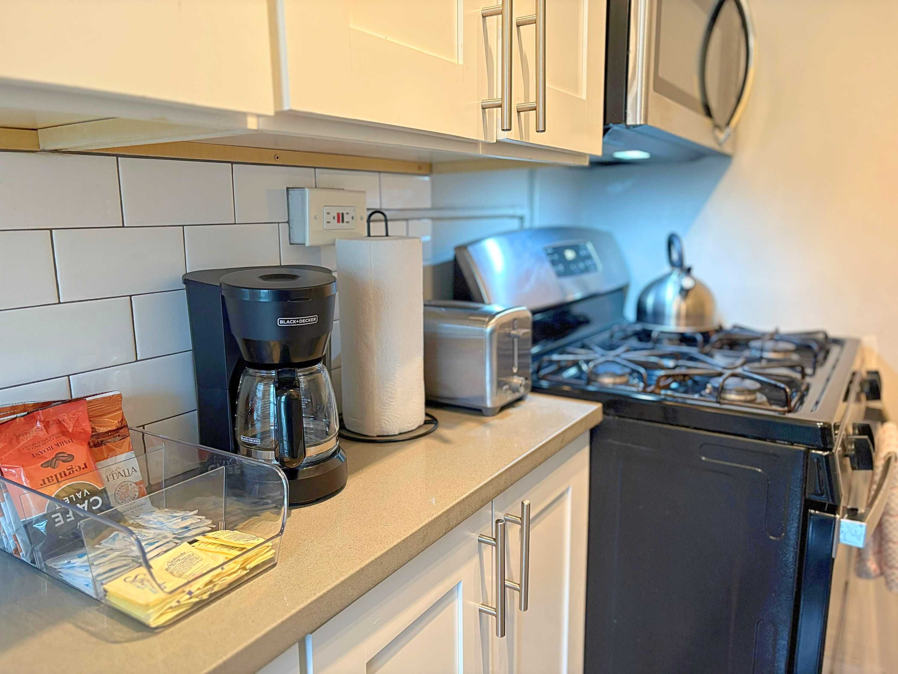 Una cocina con gabinetes blancos, cafetera, tostadora y estufa a gas.