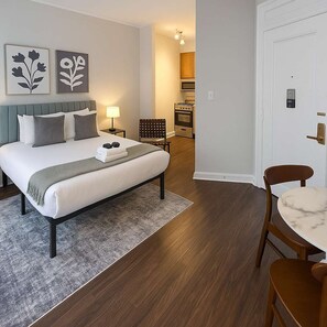 Een moderne hotelkamer met een groot bed, een zithoek met een tafel en stoelen, een kitchenette en kunst aan de muur.