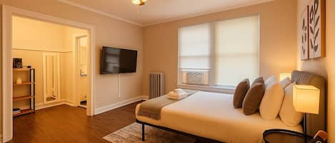 A bedroom with a bed, a TV, a ceiling fan, and a window with blinds.