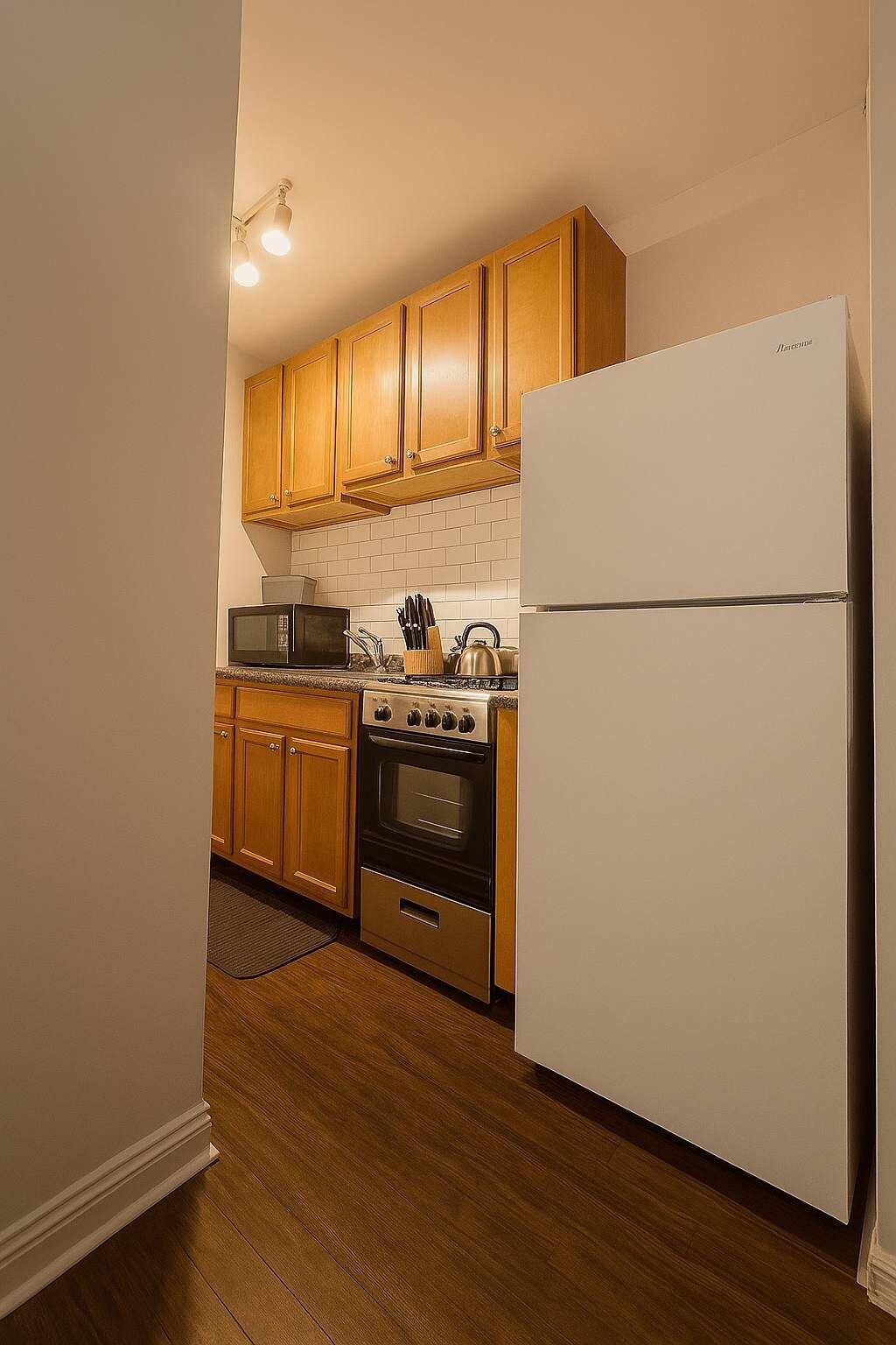 Una cocina con armarios de madera, un refrigerador de acero inoxidable, un microondas, un horno y una tetera.