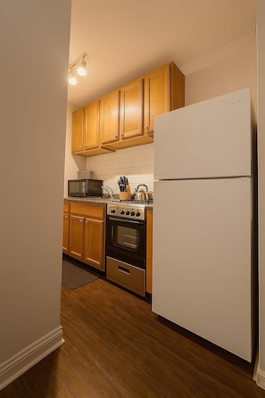 A kitchen with wooden cabinets, a stainless steel refrigerator, a microwave, an oven, and a kettle. - Cozy Charm Studio Apt in Chicago (Chicago)