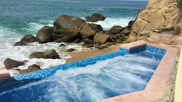 Uma banheira de hidromassagem com vista para o oceano e rochas.