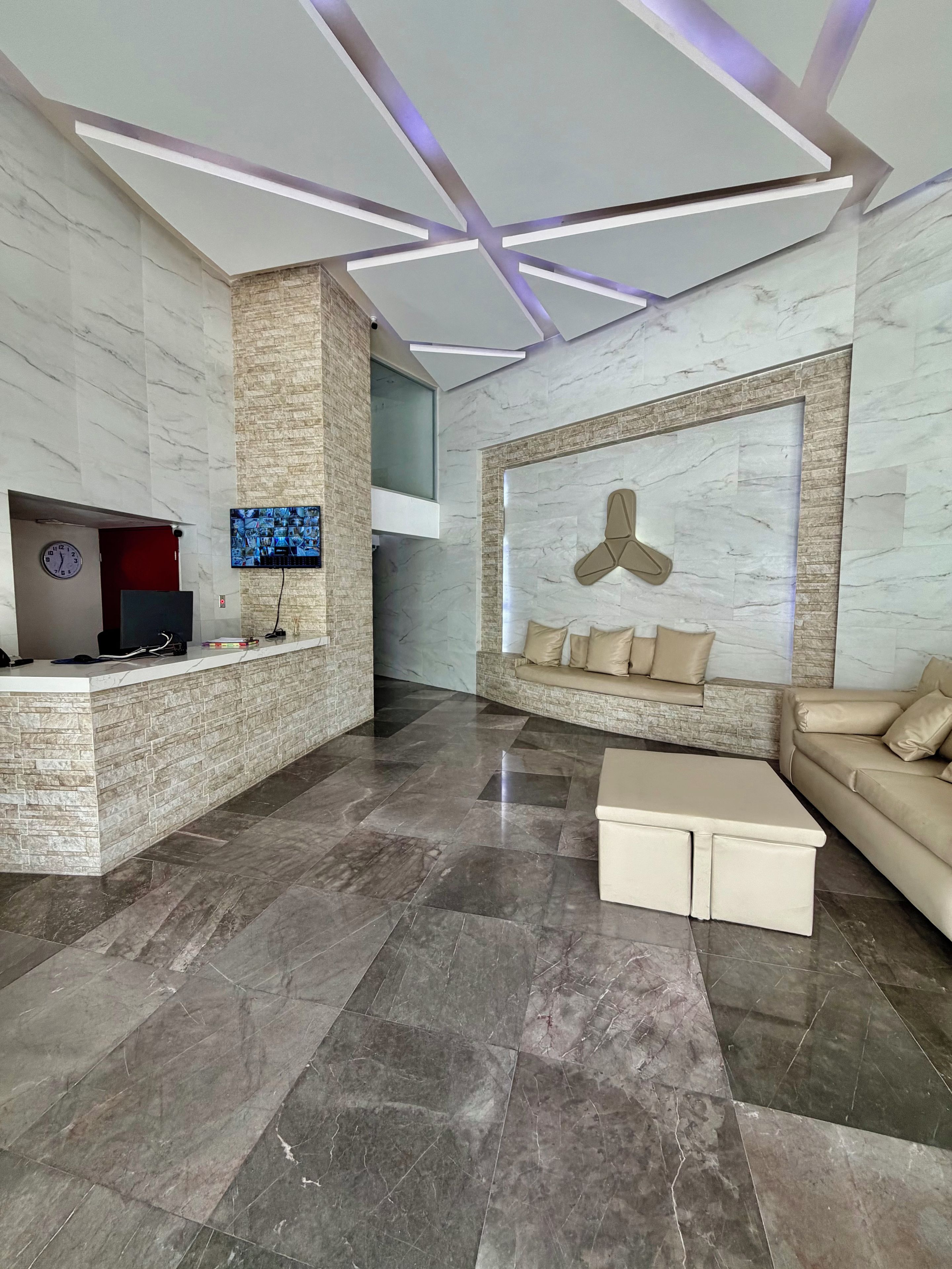 Een moderne lobby met een receptiebalie, zithoek en een groot scherm aan de muur.
