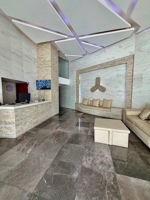 Een moderne lobby met een receptiebalie, zithoek en een groot scherm aan de muur.