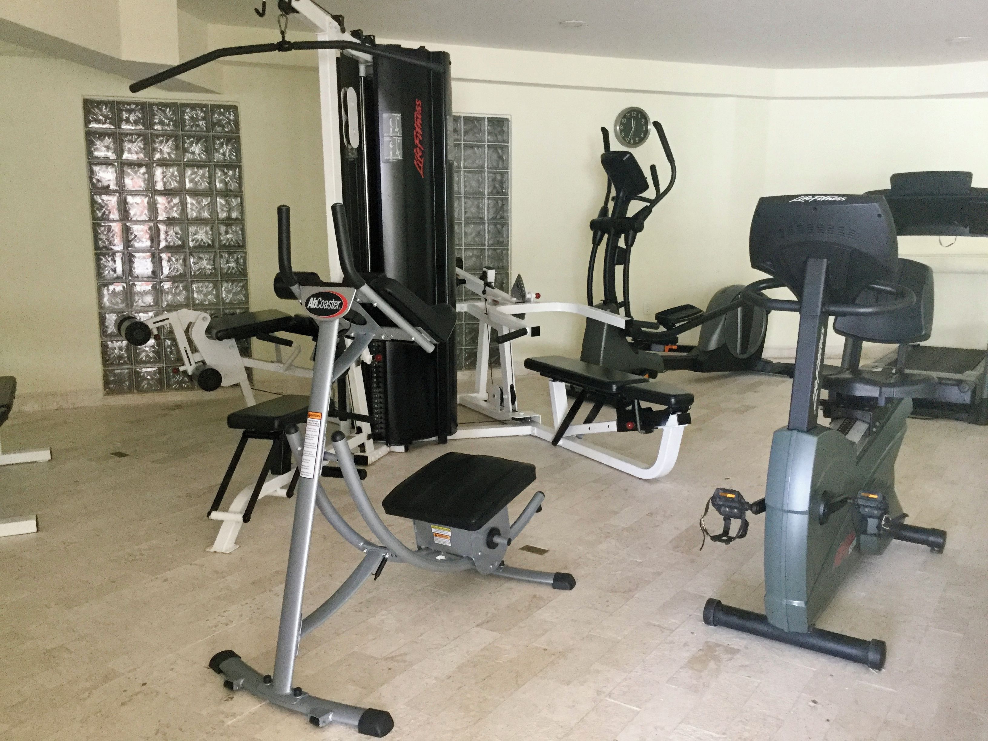 A gym with various exercise equipment including a cable machine, a bench press, and a stationary bike.