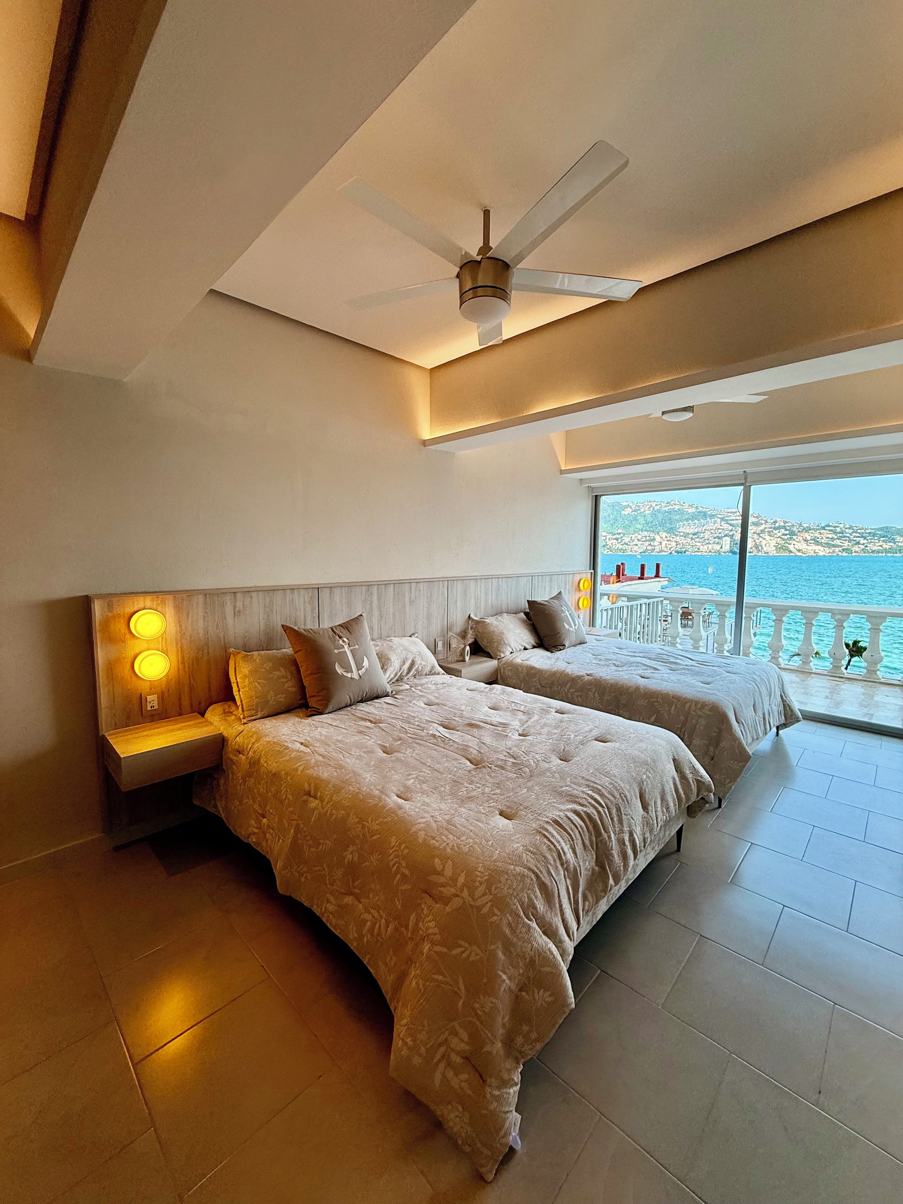 Een slaapkamer met twee bedden, een plafondventilator en uitzicht op zee.