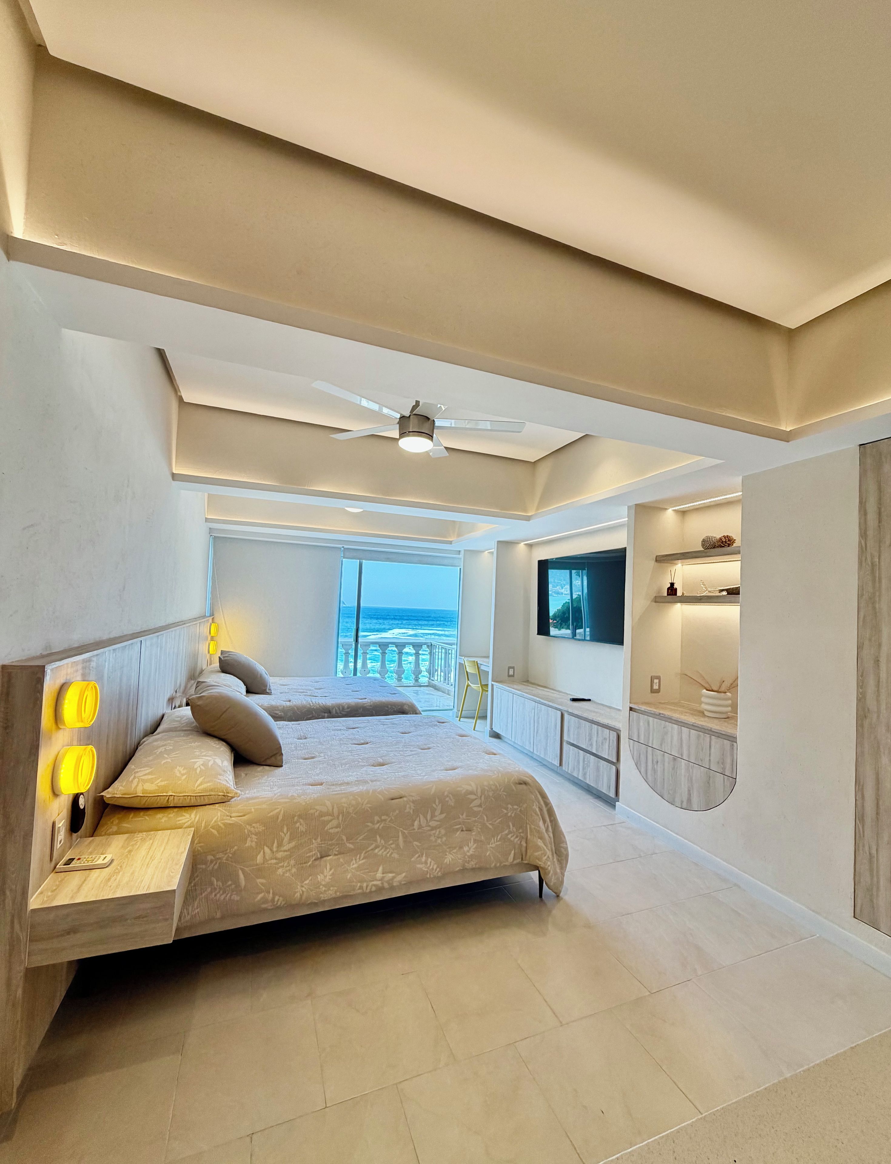 Quarto moderno com uma cama grande, ventilador de teto e vista para o oceano.