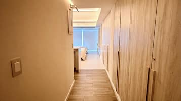 A hallway with wooden flooring, a light fixture on the left, and a closet with vertical handles on the right.