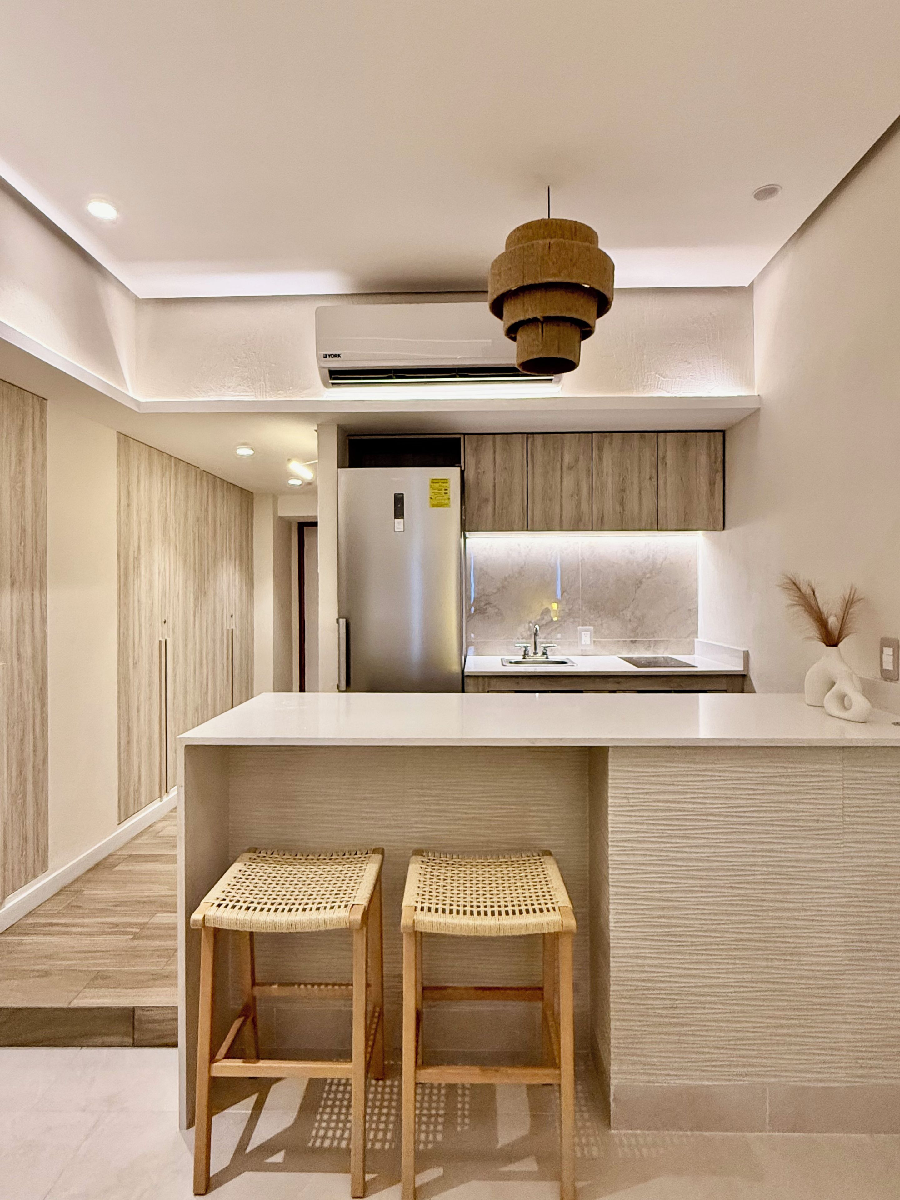 Een moderne keuken met een inbouwkoelkast, een houten kookeiland met twee krukken en een hanglamp.