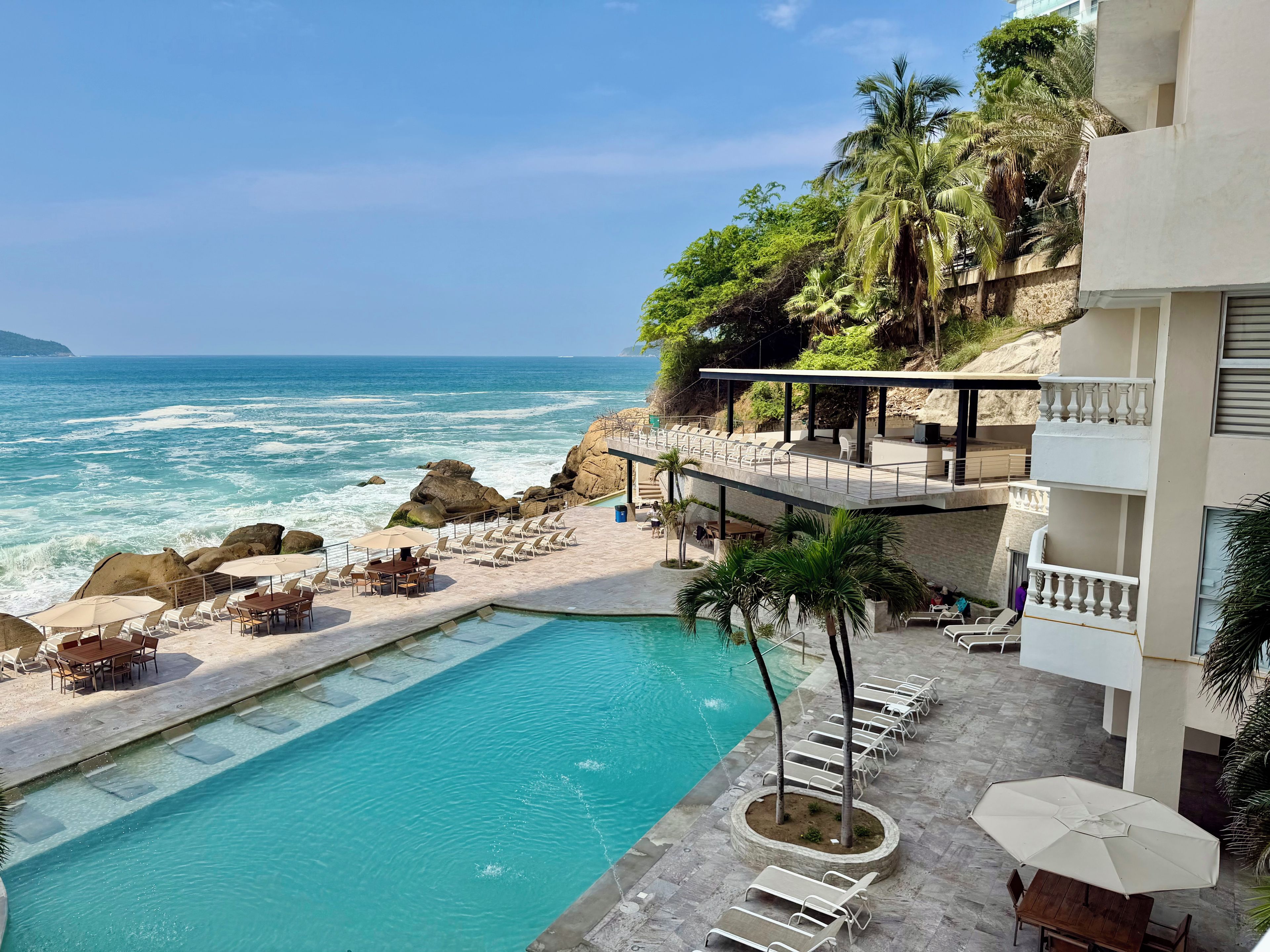 A pool area with lounge chairs and a view of the ocean.