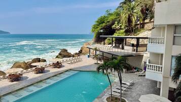A pool area with lounge chairs and a view of the ocean.