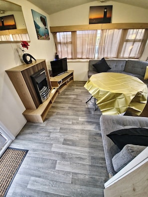 A furnished living area with a sofa, a television, a fireplace, and a dining table. - Holiday House - Sleeps 6 - Parking (Abergele)