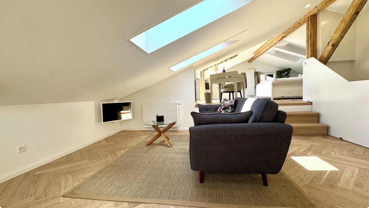 Ein modernes Loft-Zimmer mit Oberlicht, einer Couch, einem kleinen Tisch und einer Treppe zu einer erhöhten Ebene.