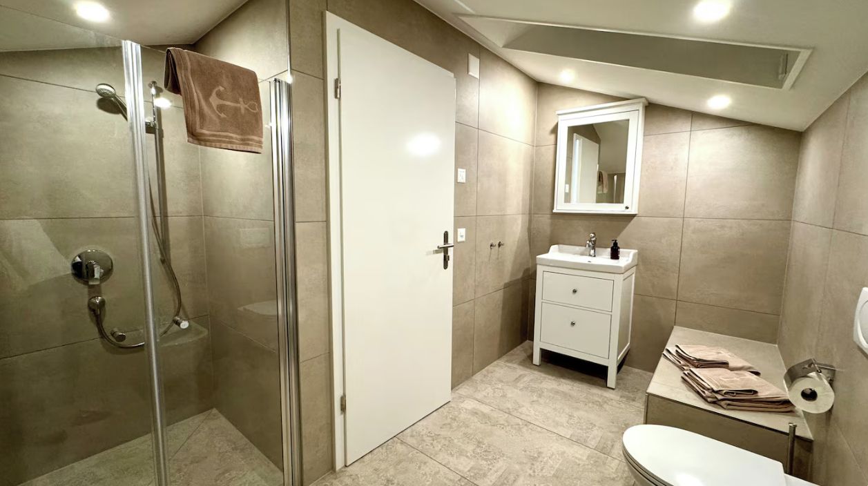 A bathroom with a glass shower enclosure, a white sink, and a toilet.