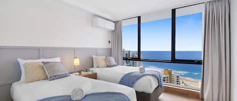 Habitación de hotel con dos camas, vista al océano y un ventanal grande.