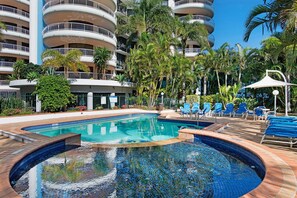 A hotel pool area with a large pool, lounge chairs, and a multi-story building with balconies. - High-Rise 2-Bed Apartment in Surfers Paradise (Surfers Paradise)