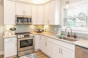 A modern kitchen with white cabinetry, stainless steel appliances, a tiled backsplash, and a window with blinds. - 6011 Rookery 3 Four Shores close to beach (Gulf Shores)