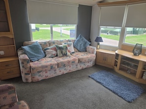 A cozy room with a patterned sofa, a blue rug, and a view of a green landscape through large windows.
