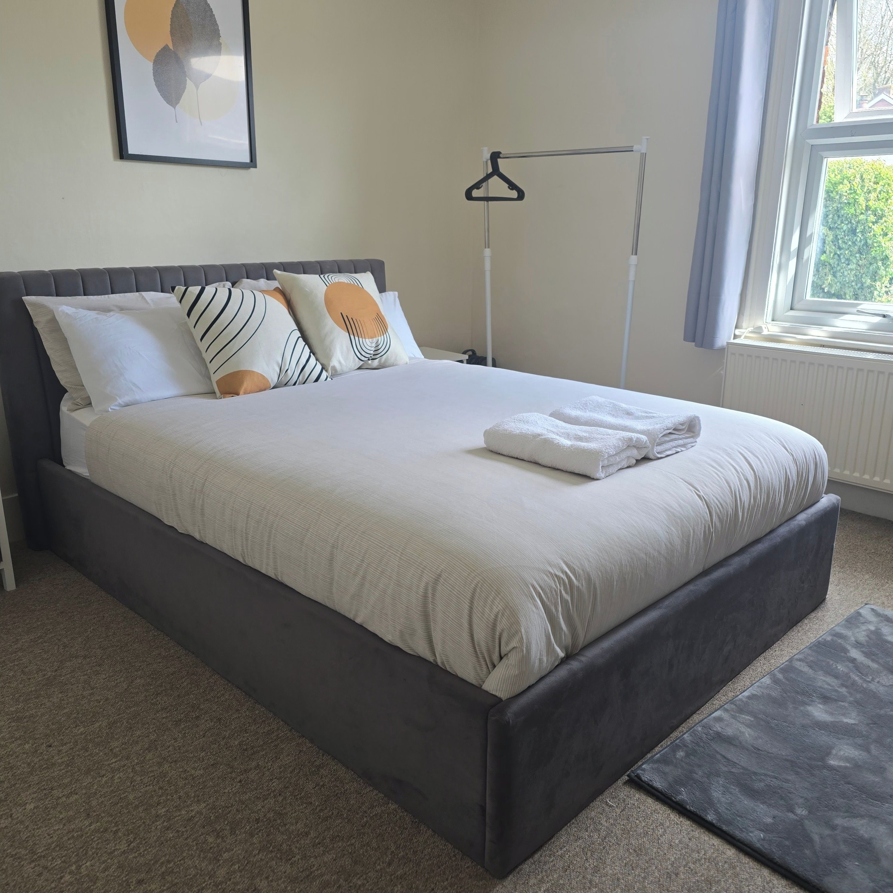 Una cama bien hecha con un cabecero gris, ropa de cama blanca y algunas almohadas estampadas.