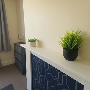 A room with a white console table, two potted plants, a grey curtain, and a black drawer unit.