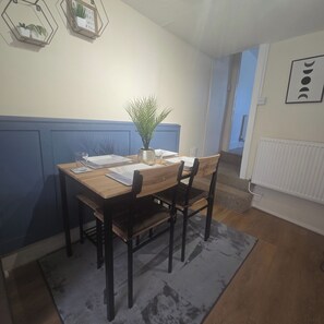 A dining area with a wooden table, two chairs, a vase with a plant, and a wall-mounted sign.