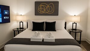 A hotel room with a bed, two bedside tables, a TV displaying the Netflix logo, and a wall art piece. - Chic Studio in Historic Hyde Park – Walk to Campus (Chicago)