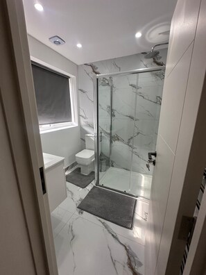 Un bany modern amb dutxa de vidre, un vàter i un lavabo.