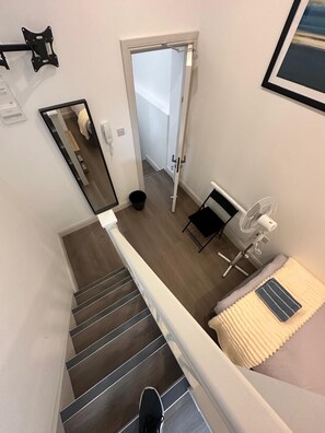 A modern interior with a staircase, a white-framed mirror, a fan, and a bed with a striped pillow. - Studio Apartment Sleeps 1 with Wifi near city (London)