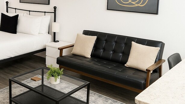 A modern hotel room with a bed, a black leather sofa, a coffee table, and a dining area. - Bright South Hyde Park Studio (Chicago)