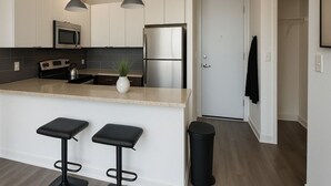 A modern kitchen with stainless steel appliances, a bar stool area, and a door leading to another room. - Bright South Hyde Park Studio (Chicago)