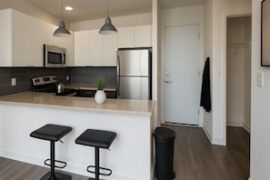 A modern kitchen with stainless steel appliances, a bar stool area, and a door leading to another room. - Bright South Hyde Park Studio (Chicago)