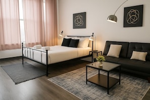 A modern bedroom with a bed, bedside tables, a sofa, and artwork on the walls. - Bright South Hyde Park Studio (Chicago)