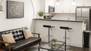 A modern living room with a leather sofa, a glass coffee table, and a black-framed bed. - Bright South Hyde Park Studio (Chicago)