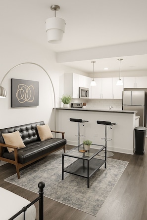 A modern living room with a leather sofa, a glass coffee table, and a black-framed bed. - Bright South Hyde Park Studio (Chicago)