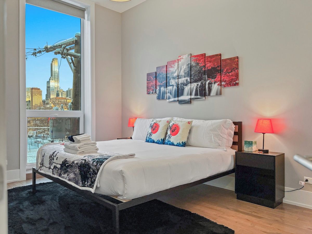 Quarto moderno com uma cama grande, vista da cidade e uma obra de arte na parede.