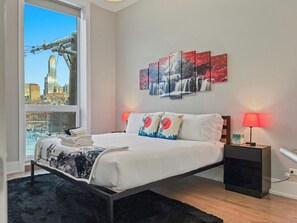 Quarto moderno com uma cama grande, vista da cidade e uma obra de arte na parede.