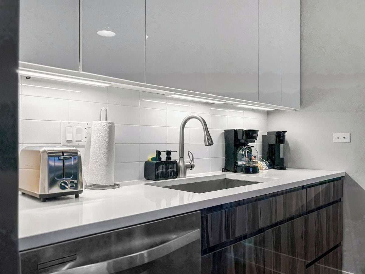 Cozinha moderna com torradeira de aço inoxidável, dispensador de toalhas de papel, cafeteira e pia com torneira moderna.
