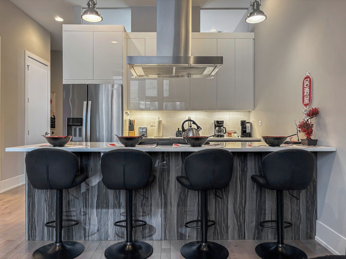 A modern kitchen with a central island, bar stools, stainless steel appliances, and pendant lighting.