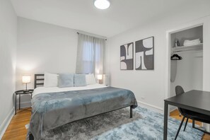 Un dormitorio con cama, mesitas de noche, escritorio y silla.