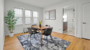 Een moderne kamer met een houten eettafel, zwarte stoelen, een potplant en een radiator.