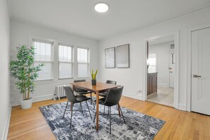 Una habitación moderna con una mesa de comedor de madera, sillas negras, una planta en maceta y un radiador.