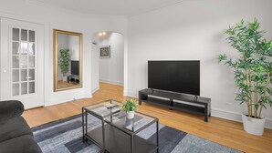 Een moderne woonkamer met een bank, een glazen salontafel, een televisie, een spiegel en een potplant.