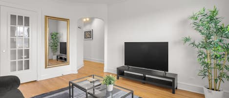 A modern living room with a sofa, a glass coffee table, a TV, a mirror, and a potted plant.