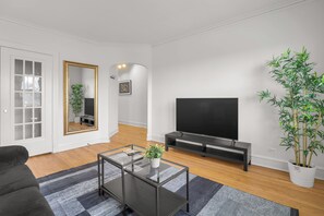 Una sala de estar moderna con un sofá, una mesa de centro de cristal, un televisor, un espejo y una planta en maceta.