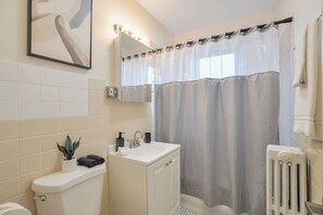Un baño con inodoro, lavamanos, armario, cortina de ducha y una planta en maceta.
