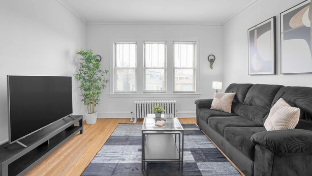 Een moderne woonkamer met een flatscreen televisie, een bank, een salontafel, een potplant en een radiator.
