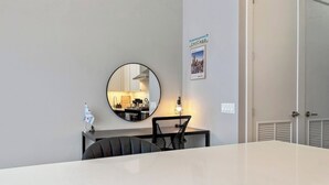 Una habitación de hotel moderna con una mesa blanca grande, un espejo redondo, una mesita con una lámpara y un cuadro enmarcado de Chicago en la pared.
