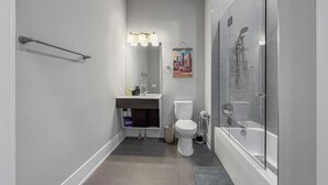 Un baño moderno con ducha de vidrio, inodoro y tocador con espejo e iluminación.