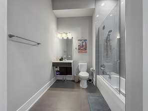 Een moderne badkamer met een douchecabine van glas, een toilet en een wastafel met spiegel en verlichting.